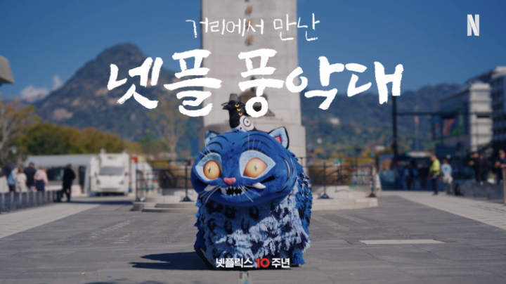 A blue papier-mâché Funak lion-dog stands in a city plaza with mountains behind it, beneath the Korean text “가리에서 만난 넷플릭스” and large brush lettering “넷플릭스 팝 코어.” The Netflix “N” logo and “넷플릭스 10 주년” are visible, matching the post’s promotion of Netflix’s Funak-themed October 24–25 celebration.