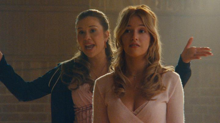 A brunette woman in a dark blazer stands behind a blonde woman in a pale pink wrap-style top, gesturing with one arm while the other looks surprised. The image fits the post’s impatient demand for “5 seasons” by suggesting the viewer wants the story or series to continue.