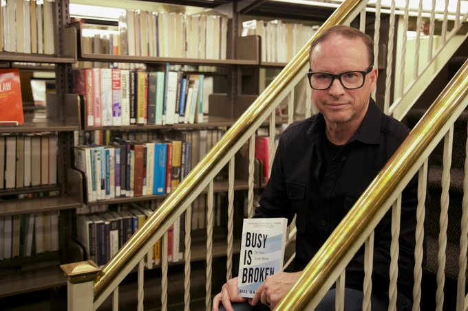Bill holding Busy Is Broken in the library stacks