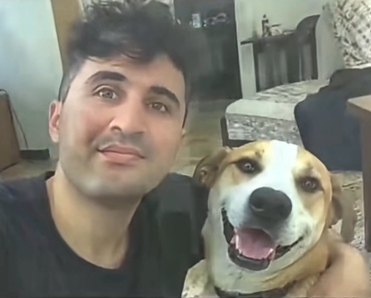 A young man poses indoors with a tan-and-white dog, both looking toward the camera with playful expressions.