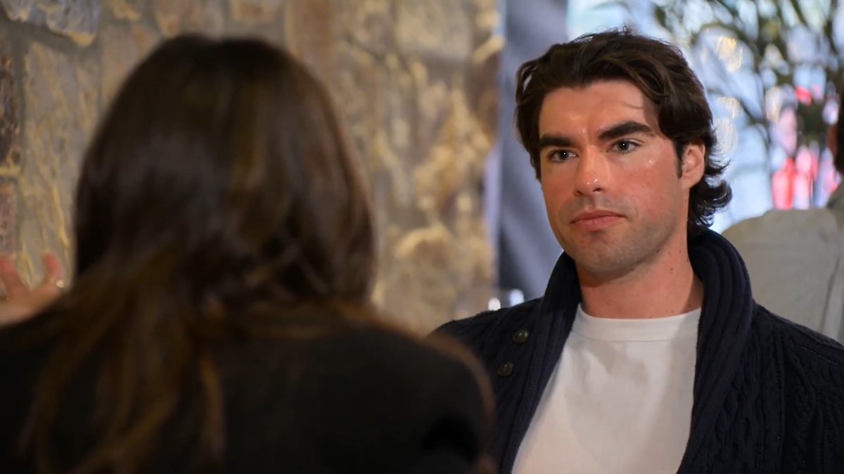 Jax, wearing a white shirt and dark cardigan, looks seriously at Stew during their reunion after she ghosted him in the pods on “Love Is Blind.” No visible text, names, numbers, or tickers appear in the image.