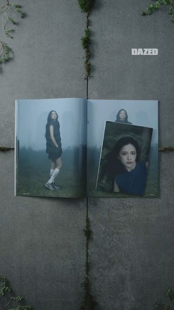 An open fashion magazine lies on gray pavement divided by mossy seams, with pages showing a woman in a misty landscape and a portrait; white text at the top right reads “DAZED.”