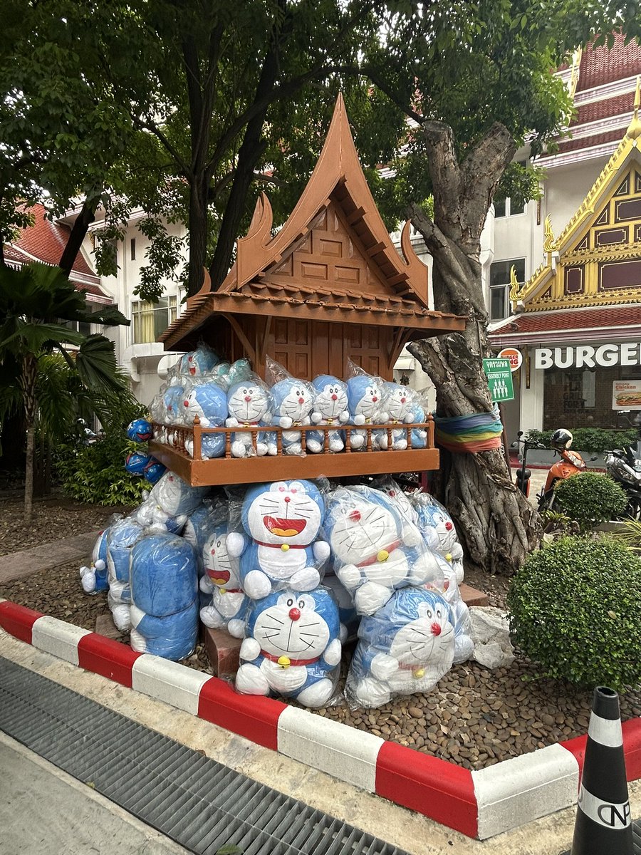 Thainews_PK's tweet photo. 【ドラえもん祠】

バンコクのモンティエン・ホテルで会議があったので、同ホテル正面玄関前の願掛け祠（通称「ドラえもん祠」）の写真を撮ってきた。

これはドラえもんを祀る祠ではない。タイ伝統の民間信仰に基づく祠で、もともとはここに宿る子供の霊に対して、願いを叶えてくれたお礼に剣や車、飛行機などのおもちゃが供えられていたのが、誰かがドラえもんを供えたのをきっかけに次第に皆ドラえもんを供えるようになった。

タイの伝統信仰と日本の現代文化の融合が面白いな。