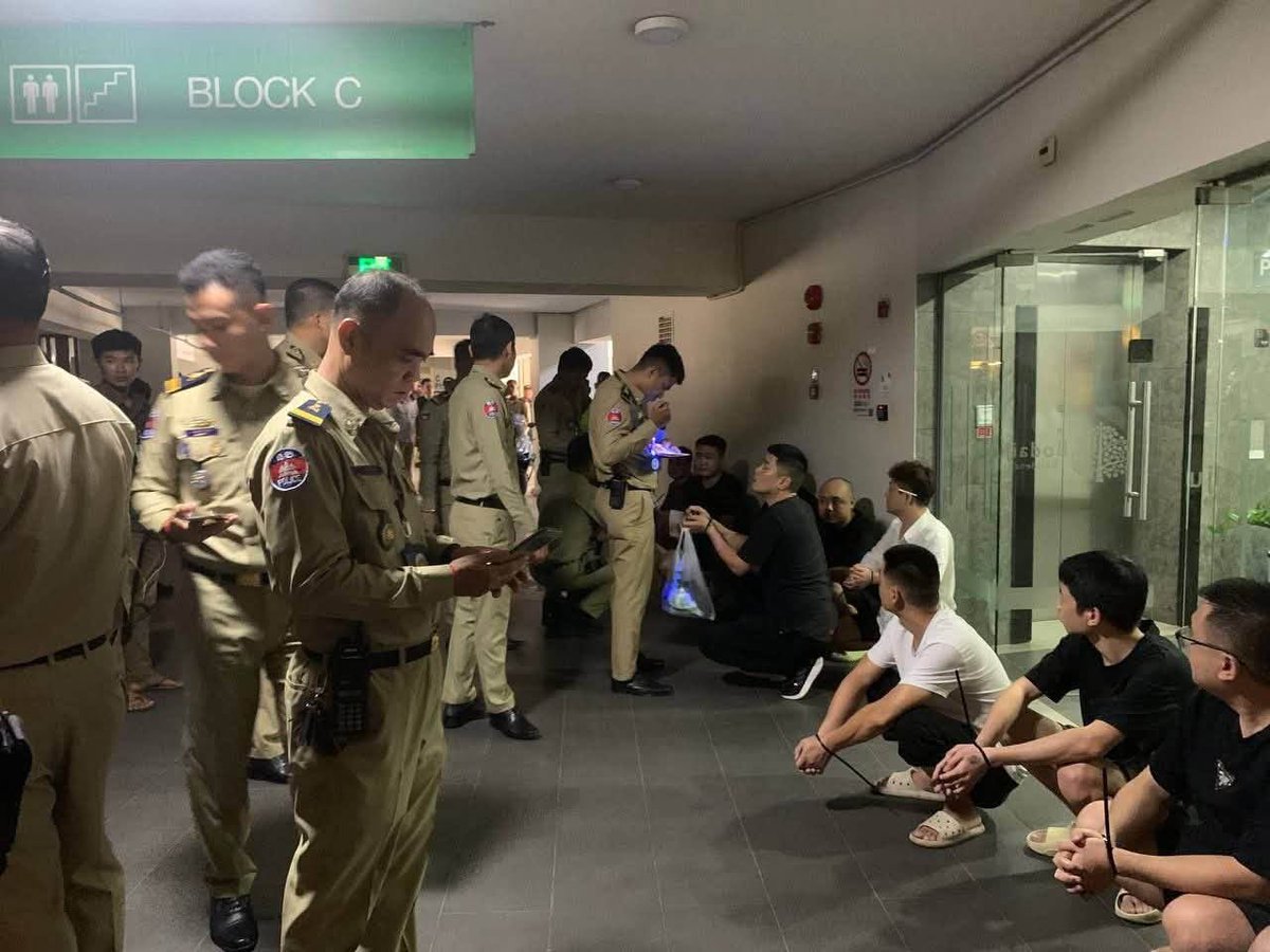 Cambodiataro's tweet photo. 【特殊詐欺ニュース】プノンペンの日系コンドミニアムでオンライン詐欺の摘発　現地メディアでは報じられない水面下の取り締まり

カンボジアの首都プノンペンにあるコンドミニアム・ボタイジュレジデンスにおいて、現地警察当局によるオンライン詐欺拠点の摘発が行われたことが、SNS上に流出した現場写真から明らかになりました。  

▪️SNSに投稿されたC棟での拘束写真と押収端末

現地の社会動向などを発信しているノアン・セレイボット氏は2026年10月22日、自身のX（旧Twitter）アカウントにて「プノンペン当局は昨日、ボダイジュ・レジデンスでオンライン詐欺の取り締まりを行った」と投稿し、2枚の現場写真を公開しました。  

公開された1枚目の写真には、同コンドミニアムの「BLOCK C」と記された緑色の案内標識がある共用廊下にて、カンボジア国家警察の制服を着た多数の警察官が取り囲む中、両手を結束バンドで縛られた複数の男性が床に座らされている様子が写っています。廊下のガラス扉には、同物件のロゴマークも確認できます。  

もう1枚の室内を撮影した写真には、木製のテーブルの上にノートパソコン5台、スマートフォン約18台、マウスや多数の充電ケーブル類、中国語の文字が記された黒い冊子などが並べられ、警察官が押収されたスマートフォンを束ねて確認している状況が記録されています。比較的小規模なグループが、一般の居住用ユニットを拠点として詐欺行為を行っていたことをうかがわせます。  

▪️プノンペン国際空港近くの大型コンドミニアム

今回摘発の現場となったボタイジュレジデンスは、プノンペン国際空港に近いポーセンチェイ区に位置しています。日本の不動産投資・開発企業であるクリードグループが開発した日系プロジェクトであり、14階建て全6棟・約900戸を有する大型コンドミニアムとして知られています。日本人投資家や現地在住者にも馴染みのある物件です。

▪️現地メディアでは報じられない摘発の実態と「公表」を分ける背景

注目すべき点として、今回の10月21日に実施されたとみられる摘発については、10月23日現在、現地主要メディアでは一切報じられていません。警察当局からの公式なプレスリリースも出されていない状況です。

カンボジアでは2025年後半から2026年にかけて政府主導のオンライン詐欺取り締まりが強化され、かつてのような大規模な専用施設での活動が困難になった結果、犯罪グループがプノンペン都内の一般のコンドミニアムやサービスアパートメントなどに小規模な単位で分散・潜伏するケースが相次いでいます。

こうした小口分散化の動きに対し、現在プノンペン都内では郊外のみならず都心部においても、コンドミニアムやサービスアパートメントに対する当局の立ち入り検査が極めて高い頻度で実施されています。実際に数多くの物件で摘発や身柄の拘束が行われていますが、そのすべてが公式に発表され、ニュースとして報じられているわけではありません。

立ち入り検査や摘発が入った際、その事実が公式発表されてメディアで一斉に報じられるか、あるいは表沙汰になることなく水面下で静かに処理されるかの分かれ目には、物件オーナーらによる当局や関係者への特別な働きかけや、相応の配慮・交渉の有無が大きく影響しているのが現地の暗黙の実情とされています。

当局は主要な摘発成果を公表する一方で、今回のように一般のコンドミニアムの1室や数室を対象とした小規模な立ち入り検査・摘発については、公式発表を行わないケースが多々あります。公式報道として可視化される事案は氷山の一角に過ぎません。

今回SNSを通じて流出した2枚の写真は、一般の高級コンドミニアムやサービスアパートメントにも詐欺グループが浸透している現状と、表向きには報じられない水面下での摘発、そして情報を巡るカンボジア特有の力学が日常的に働いているリアルな実情を静かに物語っています。