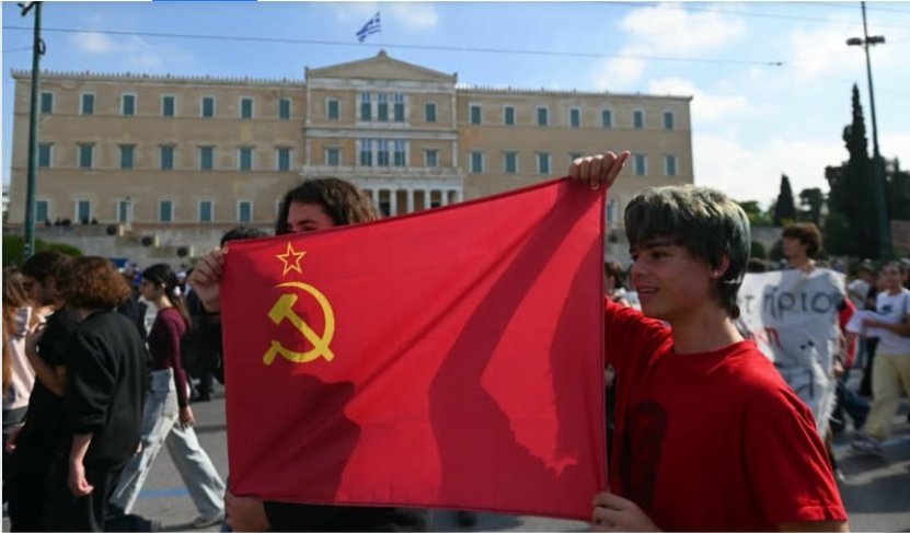 Intcomunismpic's tweet photo. 2 jóvenes sostienen la bandera Soviética frente al parlamento en las protestas de Octubre 2026 en Grecia. https://t.co/IRwSi8NT5M