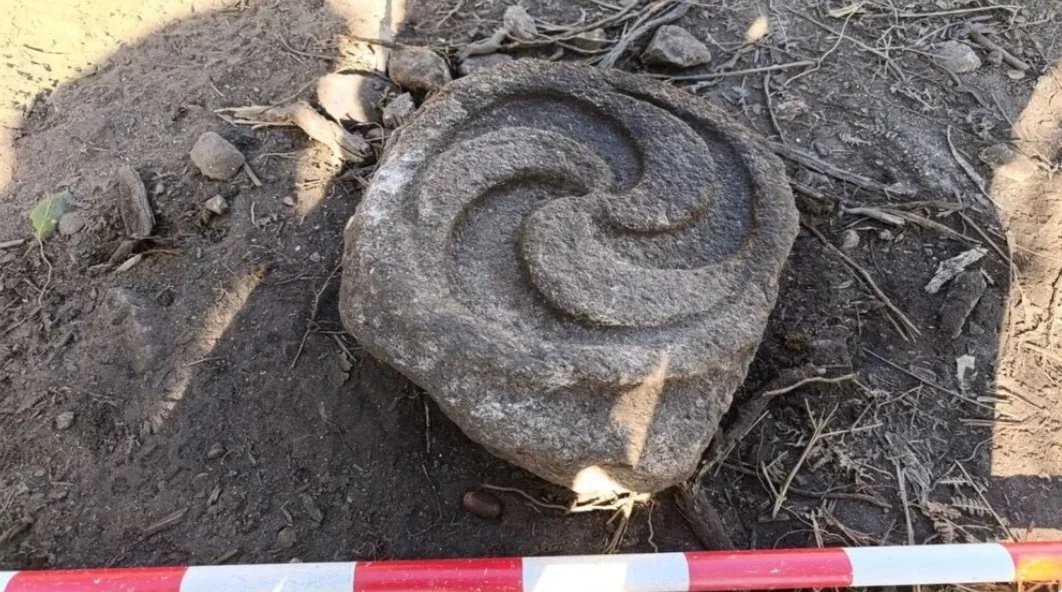 HistContent's tweet photo. A Stone With Two Faces Found in Galicia: Triskelion on One Side, Petroglyph on the Other

Archaeologists at the Castro do Pico da Bandeira in Salcidos, A Guarda (Galicia, Spain) have found a granite stone with a finely carved triskelion on one face and a rougher petroglyph on the other.

It lay inside a large circular house occupied between the 1st century BC and the 1st century AD, among fragments of Roman amphorae. The triskelion stayed almost fresh because that face fell toward the ground. Archaeologist Benito Vilas says no other stone in Galicia is known to carry both symbols on opposite sides.

Were they carved together, or did the petroglyph come first and the stone get reused later? For now the answer is open, and more than half of the house is still unexcavated.
