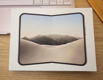 A foldable iPhone mockup displays a split-screen desert dune wallpaper on a desk. The image illustrates the post’s claim that the rumored “iPhone Duo” will feature high-end Samsung G9P foldable OLED panels.