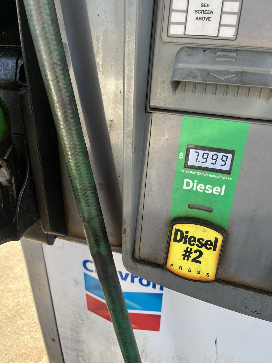 A close-up of a gas station diesel pump, with its display and fuel nozzle area visible. The pump has a green diesel label and a yellow button; a hose runs diagonally across the foreground. There is text on the pump and part of a station logo below.