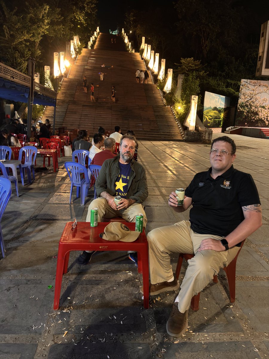 ProfTonyPollard's tweet photo. Two battlefield guides debriefing over a beer at our favourite bar in Dien Bien Phu. Behind us, the steps up the west slope of Dominique 2 - the highest of the ‘5 Hills’. https://t.co/bPPbn3ULc8