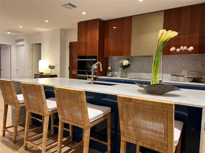 Kitchen with walnut cabinetry, a long white quartz island and woven counter stools.