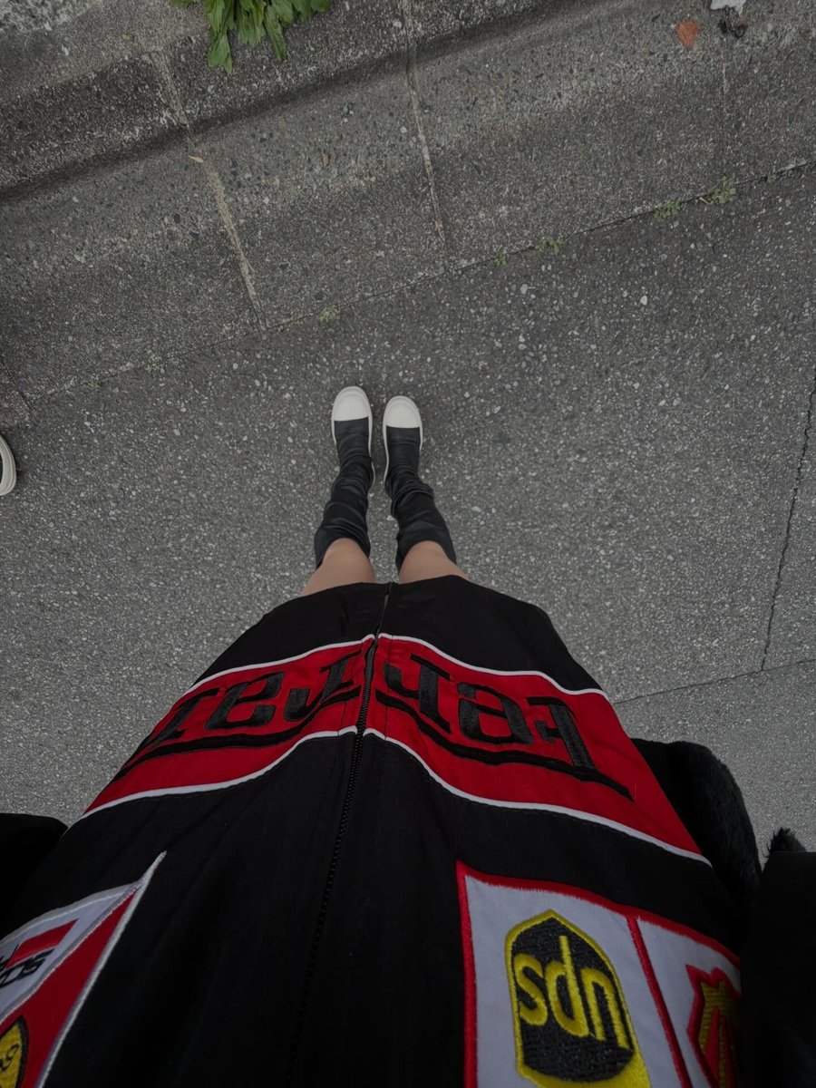 qitadera's tweet photo. down angle of me, black ferrari jacket huge, red band with black letters across my chest ˚ white-capped boots scrunched up my legs, standing on busted pavement. big jacket, little legs, y2k racer baddie on the sidewalk ⊹ https://t.co/pxEMcCWWAw