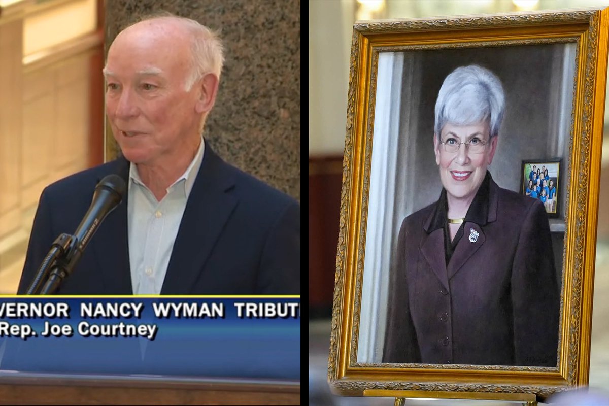 A split-screen image shows a man speaking at a microphone on the left and a framed portrait of a woman on the right. A television-style lower-third with text appears beneath the man.