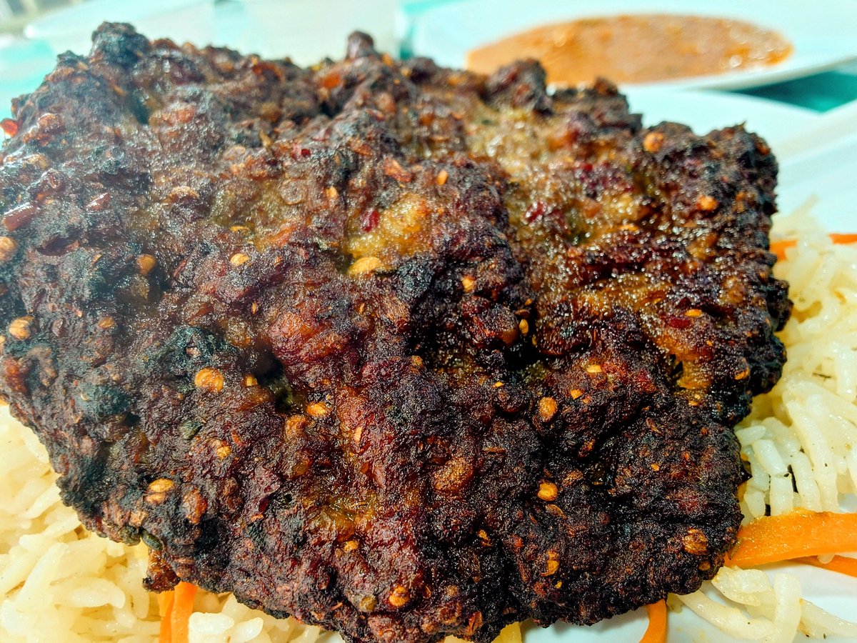 SabakuBBQ's tweet photo. 日本は「レアで」「ミディアムレアで」と、肉でも魚でも生に近いものを尊ぶ。

その対極を行くのが、チャプリ・カバブだ。

黒焦げ寸前までガリガリに焼く。表面は硬く香ばしく、脂もスパイスも一緒になって焦げる。その荒っぽさがいい。

「そんなに焼いたら肉がもったいない」ではない。そこまで焼くから、うまいのだ。

「そこがいいんじゃない！🐸」ーみうらじゅん先生 Since 1980

先日のペシャワル食堂と今日のアフガン食堂のはずいぶん違う。表面は焦げる寸前までガッツリ焼かれ、中には噛むと「ガリッ」とくるスパイス。コリアンダーシードだろうか。肉々しくて、荒っぽくて、うまい。

甘いニンジンとレーズンのプラオに謎トマトソースをかけて食べる。
これがまた、たまらない。