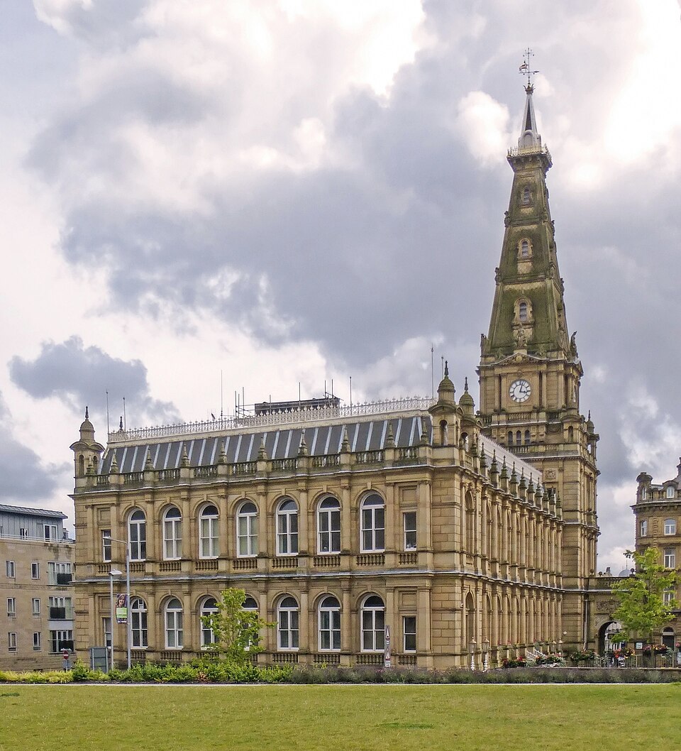 MCRReiners's tweet photo. On Northern Town Halls, and Englishness in Architecture:

Bradford's town hall (by architects Lockwood and Mawson, 1869, image 1), built in the renaissance/Italianate style, was a civic symptom of Bradford's booming mechanised worsted spinning industry. 

The bell tower is a deliberate reproduction of the Palazzo Vecchio in Firenze. The fact it still stands, given the rot of modern Bradford, is a marvel to the staying power of England's architecture. Architectural walking tours of these places will someday be the only service not outsourced to American AI. 

The North – when doing town halls –is particularly good at capturing a blend of Italianate, gothic and domestic English Vernacular palatial building. In the warmer stones of dear England. 

Image 2: Alfred Waterhouse's Manchester Town Hall, is another of these blends. Part resembling a Tudor Richmond Palace, half St Mark's in Venice. Multi-storeyed oriel windows of a Tudor mansion sit beside beside Italianate early gothic arches. 

Image 3: Chester Town Hall, by William Henry Lynn, an Irishman who won the commission in 1864. This follows a similar approach, but more in the spirit of the guildhalls of the low countries in terms of its plan – Londoners passing through might see some similarities with the Natural History Museum's two-tone Italianate masonry. 

Image 4: Halifax Town Hall – By Charles Barry & Co (completed in 1863) is something of an oddity insofar as it is executed in the sort of classical-by-way-of Sabastiano Serlio style, and in warm Ringby Sandstone, from nearby Swales Moor. Those familiar with the Tudor Burleigh house will recognise some features of its clocktower. 

We can, and shall, build these imitation wonders again. And always keep in mind, that they were imitations of greater civilisations even at the time. Many of these Northern town halls have an aura of Pugin's parliament about them – consciously in the natively English perpendicular Gothic style. Now, we have ourselves to imitate once again.