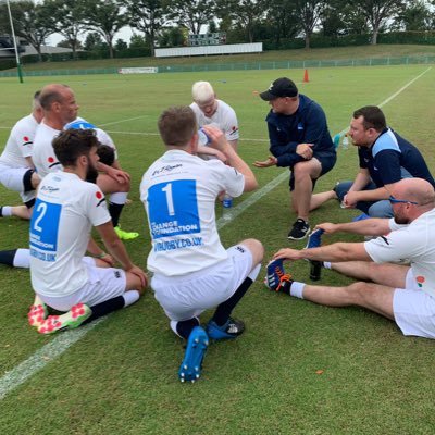 players wearing Change Foundatio t-shirts crouch together on the grassy pitch for a coaching session