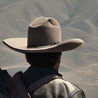 In a desolate, apocalyptic Mexico, a lone figure stands atop a craggy hill overlooking a once-bustling town now reduced to ruins.