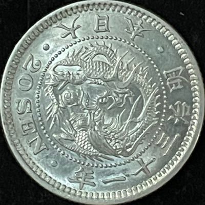 LmwPYd8k9iBtsN9's profile picture. 明治銀貨の真贋研究に長年携わる研究者。竜の“表情”と彫刻様式の差異を一瞬で見抜く。地肌・量目・比重を統合して結論を導き、細部に宿る真贋を静かに看取る。 “本物の竜は、黙って頷く”