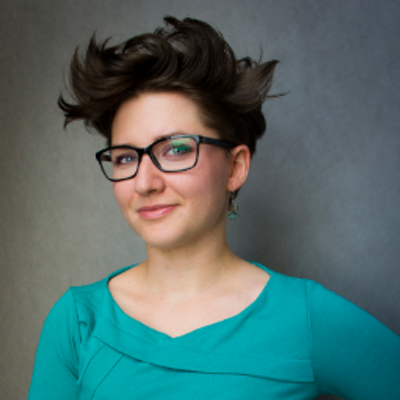 Natalia Panowicz of Codility is smiling into the camera and wearing a bright blue top against a dark grey background.