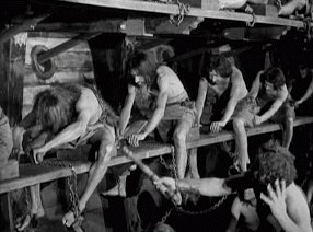 Half naked men in chains forced to row inside a ship