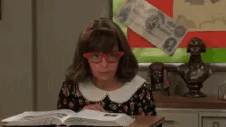 Mädchen mit großer Brille sitze hinter dickem Buch und win