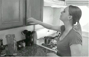 Woman opens kitchen cupboard, things fall out, she fumbles t