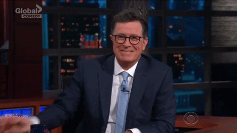 Stephen Colbert sits on the set of his talk show and holds u